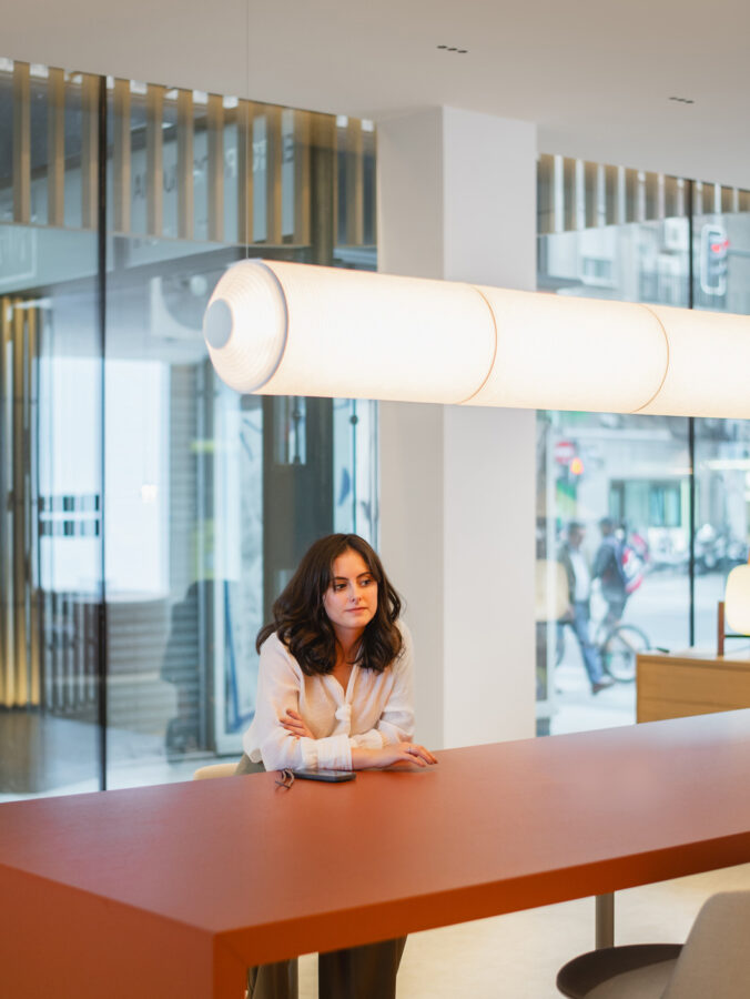 Mesa roja con lámpara de papel tubular en showroom Profusa, interior cálido y transparente