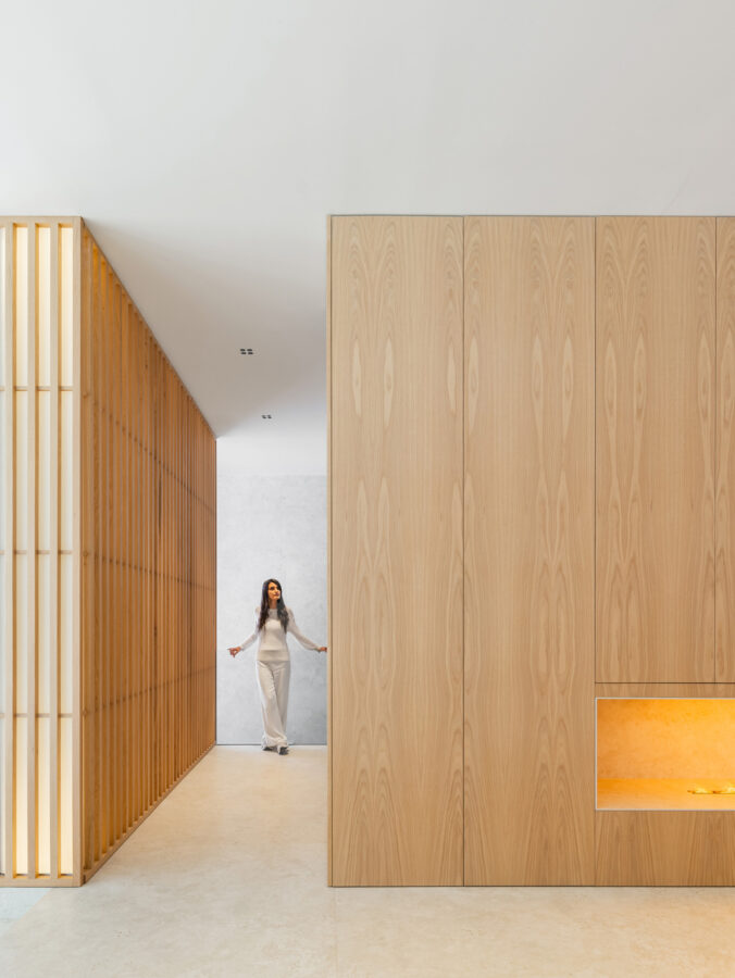 Pasillo con panelados de madera a un lado y lamas metálicas curvas iluminadas al fondo.