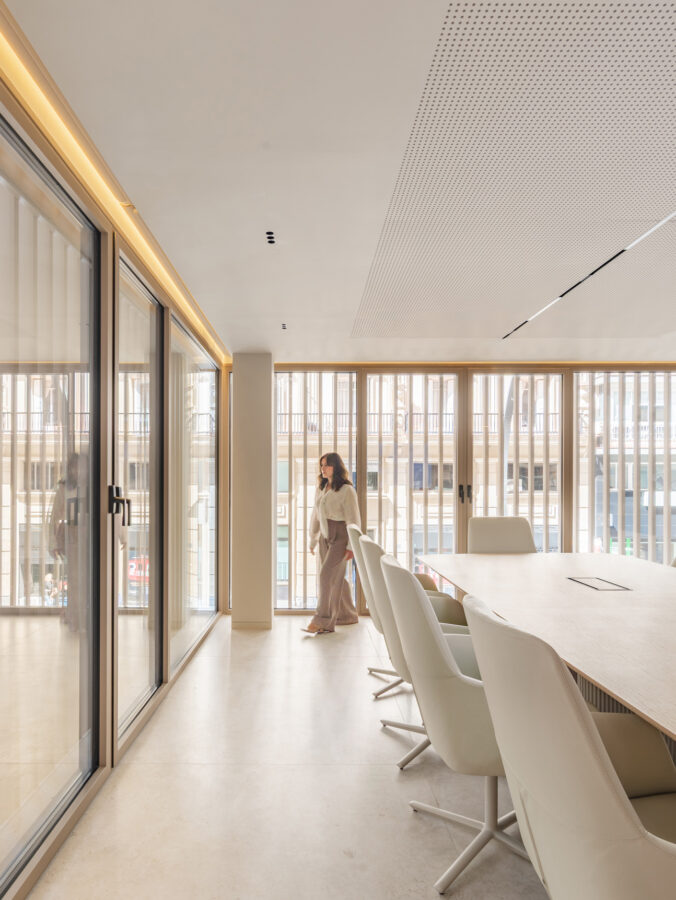 Sala de reuniones con lamas metálicas curvas en fachada y sillas de piel beige.