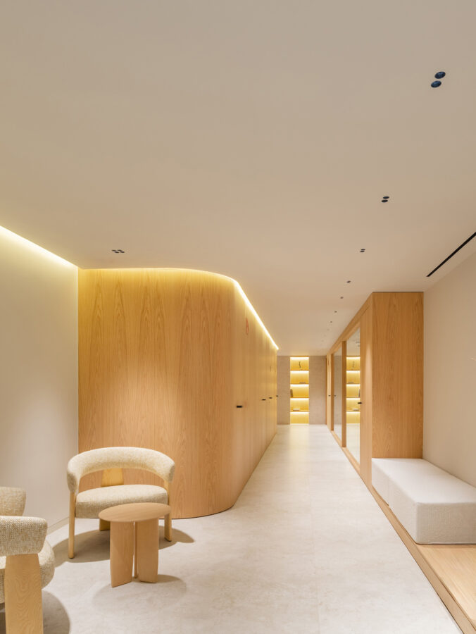 Pasillo curvo con muros de madera, banco tapizado y suelo claro.